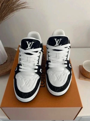 Louis Vuitton sneakers svart/vit - Säljer ett par Louis Vuitton sneakers i svart och vitt med tydlig LV-logga på plösen och präglad på tån. Skorna har snörning, rund tå och platt sula. Tillverkade i Italien med exklusiv känsla och detaljerad design. Kommer med originalkartong och dustbag. MÖTS BARA ‼️‼️