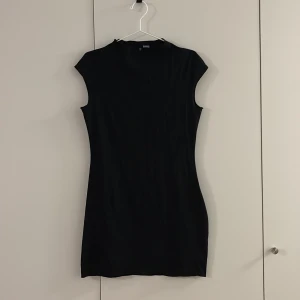 Svart ärmlös klänning från H&M Divided - Snygg svart klänning från H&M Divided i storlek M. Modellen är kort och ärmlös med en enkel, figurnära siluett och rund hals. Perfekt för dig som gillar minimalistisk stil och vill ha en klassisk look.
