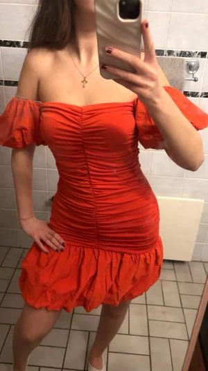 Röd offshoulder kortklänning XS/S - Säljer en röd kortklänning från H&M med offshoulder och puffiga kortärmar. Klänningen har rynkade detaljer längs hela framsidan och en volang nedtill. Materialet är lätt och känns som bomull, perfekt för att sticka ut. Passformen är tight och markerar midjan.