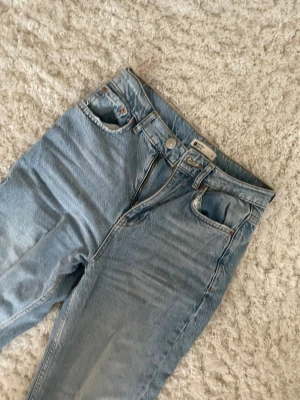 Ljusblå jeans från Gina Tricot - Säljer ett par ljusblå jeans från Gina Tricot med klassisk femficksdesign och dragkedja. Jeansen har hög midja och raka ben, vilket ger en chill och tidlös vibe. Materialet är jeans i bomull och passformen är normal. Perfekt för dig som gillar enkel och clean stil.