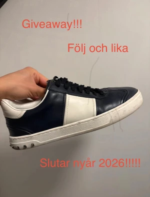 Flycrews läder  - Snygga Valentino Garavani sneakers i marinblått och vitt skinn med svarta snören och coola nitar på sulan. Klassisk rund tå och platt sula, perfekt för dig som gillar exklusiva märken och stilren design. Made in Italy.