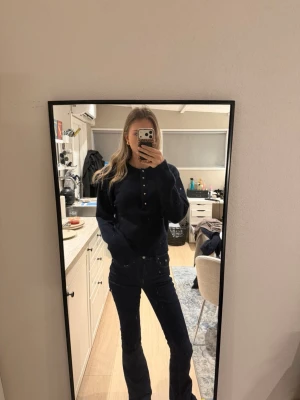 Mörkblå stickad tröja med guldknappar - Säljer en mörkblå stickad tröja med rund hals och snygga guldknappar framtill. Tröjan har lång ärm och en klassisk, enkel design som passar perfekt till jeans. Supermjuk och skön att ha på sig under kyligare dagar.