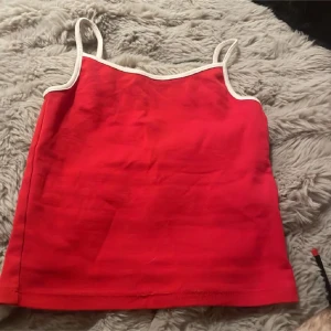 Röd linnetopp med vita kanter - Köpte för 30kr❤️ Säljer en röd linnetopp med tunna axelband och vita kanter runt halsringningen och axelbanden. Toppen har en enkel och stilren design, perfekt för varma dagar. Materialet känns mjukt och lätt mot huden.
