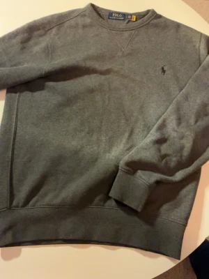 Grå sweatshirt från Polo Ralph Lauren - Säljer en stilren grå sweatshirt från Polo Ralph Lauren i storlek S. Tröjan har rund hals, lång ärm och klassisk logga broderad på bröstet. Materialet är mjuk bomull och passformen är normal, perfekt till jeans eller joggers. Modell: 175cm