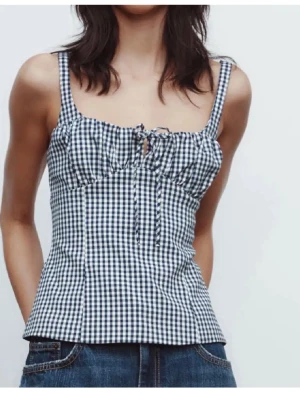 Rutig blå och vit korsett-topp Zara  - Snygg korsett-topp med blåvitt rutigt mönster och smala axelband. Toppen har en söt snörningsdetalj framtill och figurnära passform som framhäver midjan. Perfekt för dig som gillar en trendig och feminin stil.