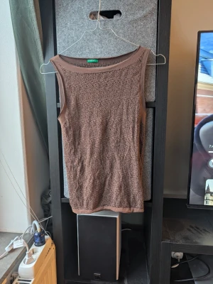 Brun ärmlös topp - Säljer en brun ärmlös topp från United Colors of Benetton. Toppen har ett snyggt virkat mönster och rund halsringning. Perfekt att matcha med jeans eller kjol för en chill look. Materialet känns mjukt och luftigt, vilket gör den skön att bära under varmare dagar.