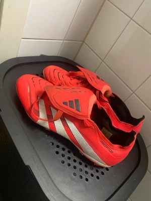 Adidas Predator röda fotbollsskor - Säljer ett par Adidas Predator fotbollsskor i röd färg med vita och svarta detaljer. Skorna har snörning, platt sula med dobbar och en klassisk Predator-tunga. Tillverkade i syntetmaterial. Perfekt för dig som vill sticka ut på planen. Bara att skriva vid en intresse och priset går såklart att diskutera!