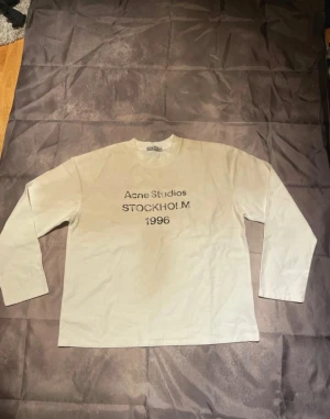Vit långärmad t-shirt Acne Studios S - Vit långärmad t-shirt från Acne Studios i storlek S. Tryck på bröstet med texten 'Acne Studios Stockholm 1996'. Tillverkad i 100% bomull, mjuk och skön med klassisk rund hals. Perfekt för dig som gillar minimalistisk och stilren design.