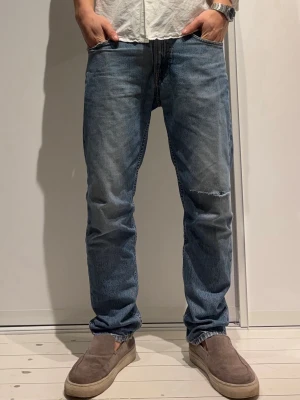  Nudie blå jeans med slitning -  Nudie jeans i klassisk blå tvätt med rak passform och normal midja. Jeansen har en fet slitning på ena knät och överlag cool stil .             Modell:Gritty jackson.                                    Färg:day dreamer.                                            Storlek: 30/30