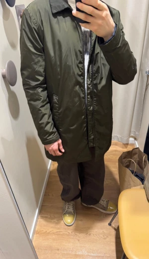 Mörkgrön vindjacka från Tiger of Sweden - Snygg mörkgrön vindjacka från Tiger of Sweden med klassisk krage och raka linjer. Jackan har dragkedja framtill, två sidofickor och är helfodrad med mörkt innerfoder. Perfekt för dig som gillar stilrena och enkla plagg.