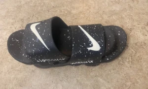 Nike Vapormax sandaler svart/vit - Svarta Nike Vapormax sandaler med vit splatter-effekt och stor vit Swoosh-logga på ovansidan. Sulan har en unik, upphöjd design som påminner om Vapormax sneakers. Materialet är syntet och sandalerna har öppen tå och platt sula. Perfekt för chill dagar och streetwear.