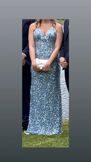 Glittrig blå långklänning med smala band - Supersnygg blå långklänning med massor av glitter och smala axelband. Djup v-ringning och figurnära passform som ger en elegant siluett. Perfekt för bal eller fest där du vill sticka ut och glänsa. Materialet är glittrigt och skimrande, vilket ger en lyxig känsla.