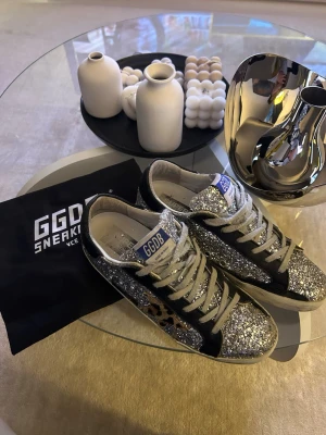 GGDB glittriga sneakers med leoparddetalj - Hej!😊Säljer ett par fina GGDB sneakers med silverglittrigt yttre. | Stolrek:38| Skick-9/10- lite smuts vid sulan som går o tvätta bort enkelt. Säljer dom för ett relativt passande pris utifrån skicket. Box och goodie bag kommer till~ DMa✨