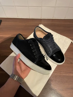 Lanvins - Snygga svarta sneakers från Lanvin med vit platt sula och lackad tå. Skorna ör i otroligt bra skick då man ser knappt på användning. Skorna är i storlek 41 men står i skon att det är uk5 men passar som de ska på en storlek 41. Priset är inte hugget i sten och går att förhandla.
