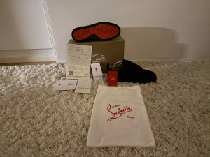 Christian Louboutin svarta sneakers - Svarta sneakers från Christian Louboutin med ikonisk röd sula och rund tå. Skorna har snörning och är tillverkade i mocka med platt sula. Medföljer originalkartong, dustbag och äkthetsbevis. Perfekt för dig som gillar lyxiga detaljer och stilren design.