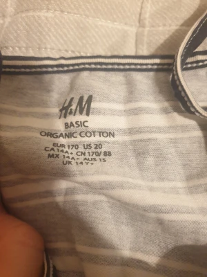 Randig långklänning från H&M - Säljer en snygg långklänning från H&M i ekologisk bomull. Klänningen har smala axelband och ett elastiskt midjeparti. Mönstret är randigt i marinblått och vitt, vilket ger en fräsch och ungdomlig look. Perfekt för varma dagar och enkel att styla med sneakers eller sandaler.