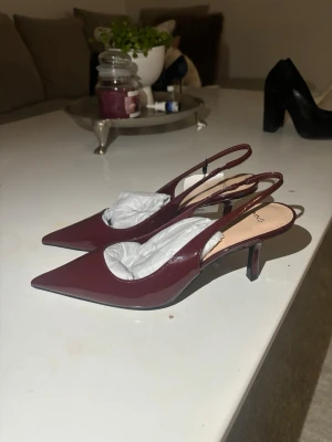 Vinröda pumps med spetsig tå från MNG - Säljer ett par stilrena vinröda pumps från MNG med spetsig tå och öppen häl. Skorna har en låg klack och är gjorda i glansigt syntetmaterial. Perfekt för dig som gillar eleganta och trendiga skor med en modern touch.