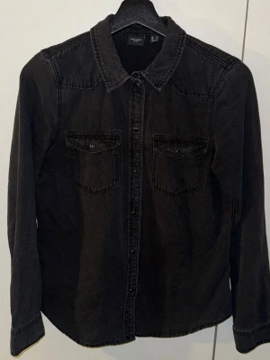 Svart jeansjacka från Vero Moda - Svart jeansjacka från Vero Moda med klassisk krage, två bröstfickor med knappar och långa ärmar. Jackan har en rak passform och är tillverkad i denim. Perfekt för dig som gillar en enkel och stilren look.