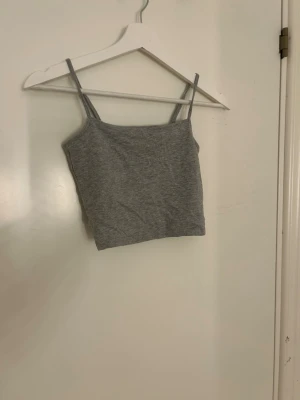 Grå croppad linnetopp från 157 - Säljer en enkel och stilren grå croppad linnetopp från 157 med smala axelband. Toppen är tillverkad i mjuk bomullsmix med viskos och elastan för extra stretch. Perfekt för varma dagar eller som layering-piece.