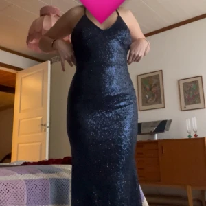 Mörkblå glittrig långklänning - Snygg mörkblå långklänning med glittriga paljetter över hela klänningen. Modellen är figurnära och har öppen rygg med smala axelband. Perfekt för dig som vill sticka ut med en glam look. Materialet är troligtvis polyester med paljettapplikationer. Är i nyskick. Skicka om du vill ha mer bilder
