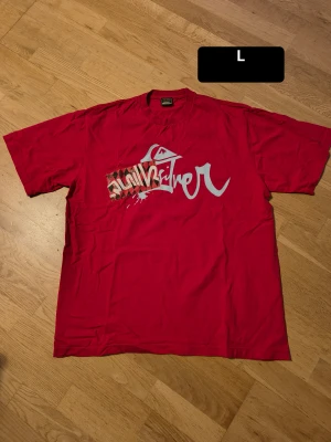 Röd Quiksilver t-shirt med tryck - Säljer en röd t-shirt från Quiksilver i storlek L. T-shirten har ett stort grafiskt tryck med logga och mönstrad detalj på bröstet samt mindre tryck på ryggen. Klassisk rund hals och korta ärmar. Materialet är mjuk bomull, perfekt för chill dagar.