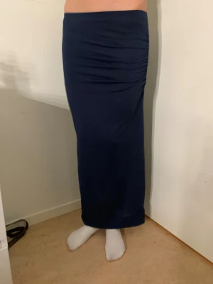 Mörkblå långkjol med slits💘 - Säljer en mörkblå långkjol med snygg rynkning på sidan och en diskret slits för extra rörelsefrihet. Kjolen har en tight passform och är gjord i mjukt, stretchigt material som sitter skönt mot kroppen. Perfekt att styla med crop tops eller sneakers.💞