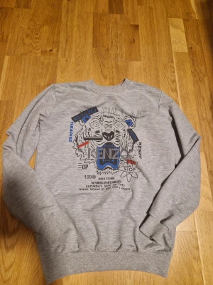 Grå Kenzo sweatshirt med tigertryck - Säljer en grå sweatshirt från Kenzo i storlek XL i barn. Perfekt för dig som gillar streetwear och snygga prints.
