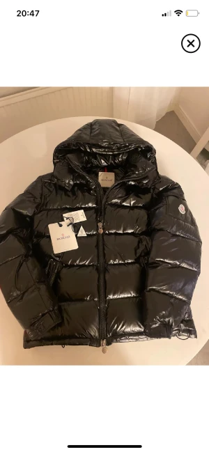  Moncler Maya - Säljer en svart  Moncler Maya med glansig finish och huva. Jackan har Moncler-logga på ärmen, dragkedja framtill och quiltad design. Perfekt för dig som vill ha en snygg och varm jacka med street-vibe. Fylld med dun och har coola detaljer som märkestaggar och justerbara muddar, NFC Scan.❄️skriv för mer frågor 🤝🏼⛷️