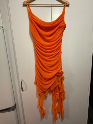 orange klänning med volanger - orange, stretchig och åtsittande klänning med volanger från shein! klänningen har justerbara axelband, en blomdetalj vid ena sidan samt en ribbad sömn vid midjan. aldrig använd, endast testad