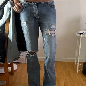 Blå bootcut jeans med nitar och slitningar - Säljer ett par blå bootcut jeans med rå kant upptill och slitna detaljer på benen. Jeansen har silverfärgade nitar längs sidorna. Står ej storlek men skulle säga S/W26/27 och passar mig bra i längden som är 170cm. 