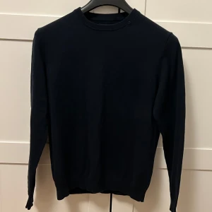 Replay tröja - Säljer en stilren mörkblå stickad tröja från Replay i premium bomull. Tröjan har ett litet Replay emblem vid halsringen. Storlek S (passar ungefär mellan 160-175)