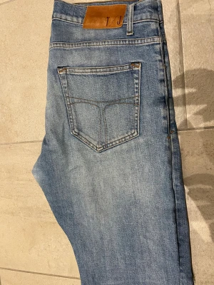 Ljusblå jeans Pistolero 32/32 - Säljer ett par ljusblå jeans från Pistolero i klassisk femficksmodell. Jeansen har raka ben, normal passform och snygga slitningar framtill för en avslappnad look. Tillverkade i bomull med läderpatch bak i midjan. Perfekta till vardagsstilen.