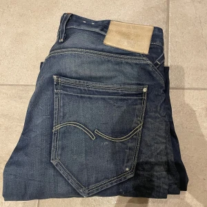 Jack and jones mörkblå jeans - Säljer ett par Jack and jones jeans i mörkblå tvätt med klassiska kontrastsömmar och läderpatch bak i midjan. Modellen har raka ben och fem fickor, med snygga detaljer på bakfickorna. Perfekt för dig som gillar tidlös denimstil. Storlek 34/34
