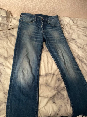 G-Star RAW 3301 Straight jeans blå - Säljer ett par G-Star RAW 3301 Straight jeans i klassisk blå tvätt med snygga slitningar och kontrastsömmar. Modellen har raka ben, fem fickor och läderpatch med logga bak. Perfekta för dig som gillar street och casual stil.