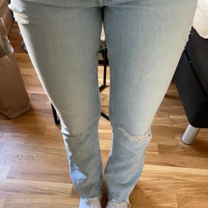 Ljusblå slitna straight jeans - Säljer ett par ljusblå jeans med slitningar vid knä och lår samt fransade benslut. Jeansen har klassisk femficksmodell, rak passform och normal midja. Perfekta för en avslappnad och trendig look.
