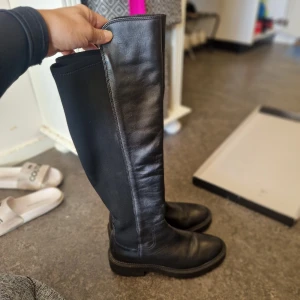 Svarta höga stövlar "Nero" i skinn fr Ella of Sweden str 40 - Säljer ett par svarta höga stövlar med chunky sula och dragkedja på insidan. Ovandelen är i en kombination av skinn och baksidan av stretchig textil, vilket ger en snygg och bekväm passform. Nypris 1899