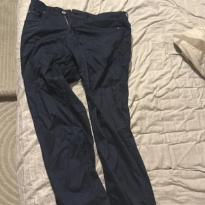 Mörkblå kostymbyxor från BOSS - Snygga mörkblå kostymbyxor från BOSS med diskret geometriskt mönster och röda detaljer på insidan av linningen. Byxorna har klassisk passform, dragkedja och knapp framtill samt stretchigt material för extra komfort.