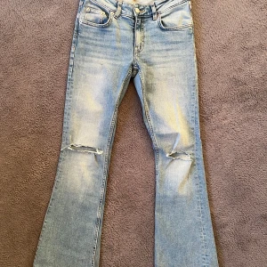 Ljusblå boot cut jeans med hål - Bootcut jeans från 157 i ljusblå färg med slitningar och hål vid benen. Jeansen har en lätt utsvängd passform nertill och är i storlek xs. Finns tecken på användning nertill på jeansen då man gått på dem 