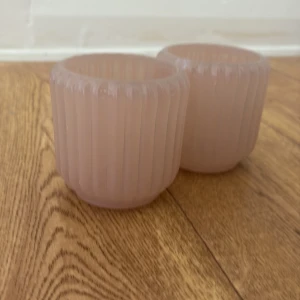 Ljushållare  - Bilderna visar två rosa glaslyktor med räfflad yta och rund form. De ser ut att vara i gott skick utan synliga skador eller slitage. Perfekta som ljushållare eller dekorativa glas för hemmet. Säljs som ett par.