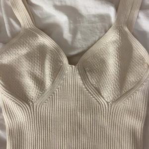 Beige ribbad linnetopp Gina Tricot - Säljer en beige ribbad linnetopp från Gina Tricot. Toppen har breda axelband, markerade kupor med stickad struktur och en tight passform. Materialet är stickat och stretchigt, perfekt för en trendig och clean look.