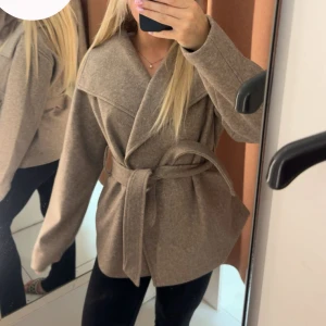 Beige omlottjacka med bälte - Snygg beige kappa från gina, den har ett matchande bälte i midjan. Perfekt för lager-på-lager och har långa ärmar. 