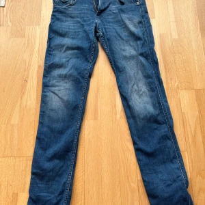 Replay Hypetflex Anbass slim fit strl 28waist 33 längd - Säljer ett par klassiska blå jeans från Replay med raka ben och snygga detaljer på bakfickorna. Jeansen har normal passform och är tillverkade i slitstarkt denimtyg. Perfekta för dig som gillar en tidlös look med lite streetkänsla.