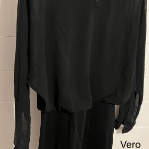 Svart klänning med glittrig v-ringning - Säljer en svart, luftig klänning från Vero Moda med transparenta, långa ärmar och glittrig v-ringad krage.