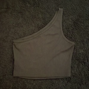 Svart one shoulder topp från SHEIN - Säljer en fin svart ribbad  one shoulder topp från SHEIN i storlek S. Toppen är croppad och har en asymmetrisk design med en axel. Materialet är mjukt och stretchigt.💕