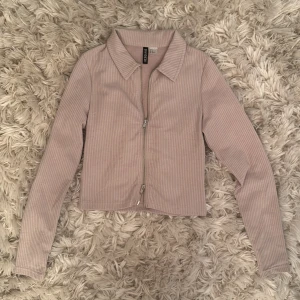 Beige ribbad kofta från H&M Divided - Säljer en beige ribbad kofta från H&M Divided i storlek S. Koftan har lång ärm, krage och hel dragkedja framtill. Materialet är mjukt och stretchigt, perfekt för lager-på-lager. Enkel och clean stil som passar till allt.
