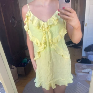 Gul volangklänning med smala axelband - Säljer en söt gul klänning med smala axelband och volangdetaljer både framtill och längs nederkanten. Nyskick! 