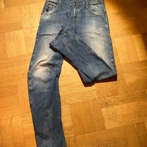 Blå jeans från G-Star RAW - Säljer ett par klassiska blå jeans från G-Star RAW med snyggt slitna detaljer och ljus tvätt. Jeansen har raka ben och en fet g-star patch bak i midjan. Materialet är robust denim i bomull och passformen är normal. slitningarna är riktigt fina trots att dom knappt är använda , har haft på mig dem ändast 2-3 gånger. Jag säljer dom för att dom helt enkelt inte passade