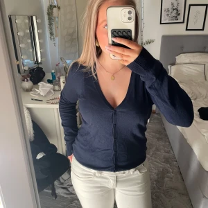 Mörkblå kofta med v-ringning - Mörkblå kofta från Kappahl med djup v-ringning och knappar framtill. Långärmad och i tunn, mjuk bomullsblandning som passar perfekt till lager-på-lager. Enkel och stilren design som funkar till det mesta.