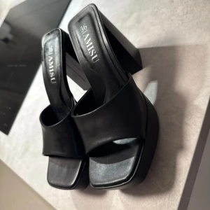 Svarta platåklackar från Amisu - Säljer ett par svarta platåklackar från Amisu i storlek 36. Skorna har bred rem över foten, fyrkantig tå och hög blockklack. Tillverkade i syntetmaterial med stilren och minimalistisk look, perfekta för att lyfta din outfit.