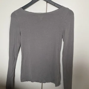 Grå långärmad topp med båtringning - En enkel och stilren genomskinlig grå långärmad topp med båtringad hals. Modellen är tight och har raka ärmar samt lätt vågig nederkant. Perfekt att styla med jeans eller kjol för en clean look.